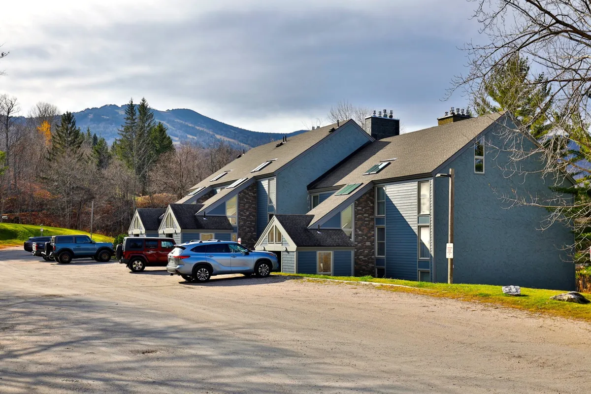 This exterior image showcases the townhouse's architecture with a dramatic mountain backdrop and a visible vehicle parking area. The scene captures the proximity to the slopes and conveys the convenience of access for guests, suggesting an easy transition from lodging to mountain adventure.