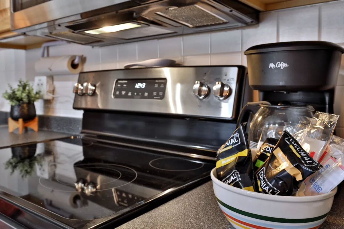 A close-up view of the kitchen’s stainless steel stove and coffee maker, with a bowl of coffee packets and a green plant for a fresh accent. The setup emphasizes breakfast or coffee time convenience and the kitchen's thoughtful details.