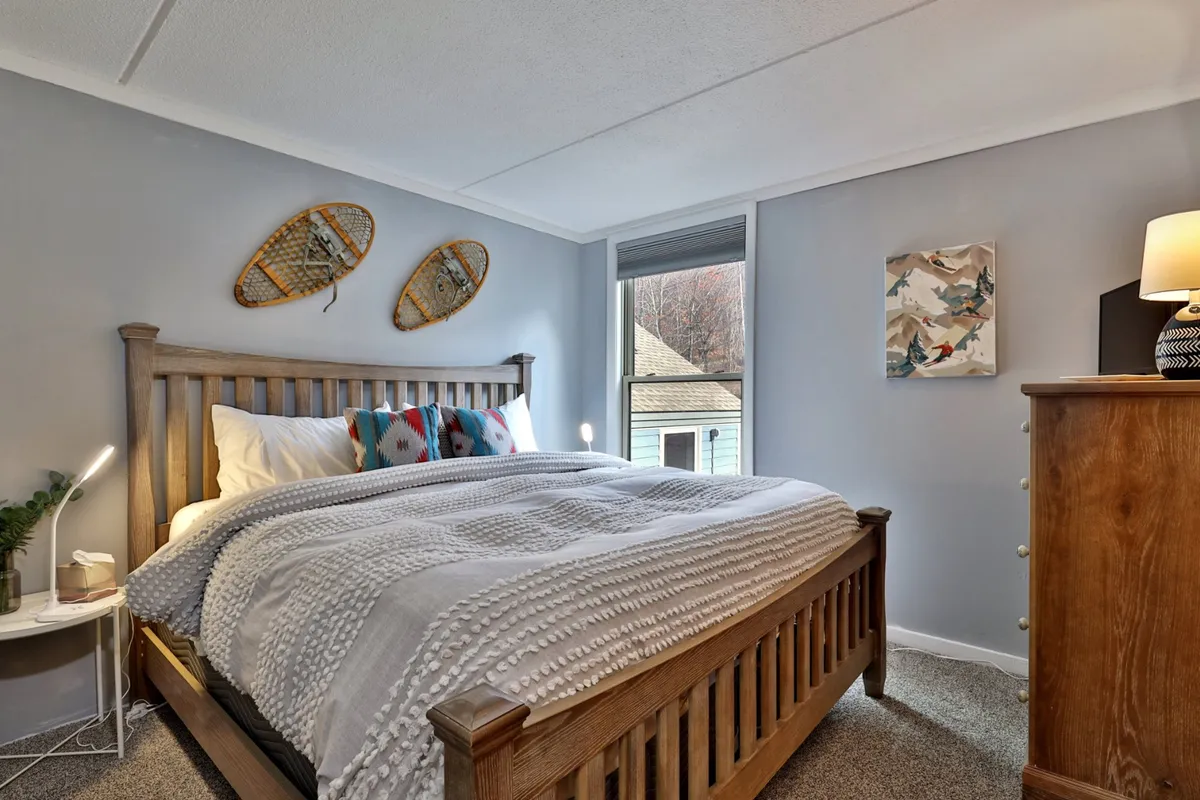 A cozy bedroom with a wooden bed frame, colorful throw pillows, wall art, and a nightstand with a lamp. The room feels welcoming and restful—ideal for winding down after a long day.