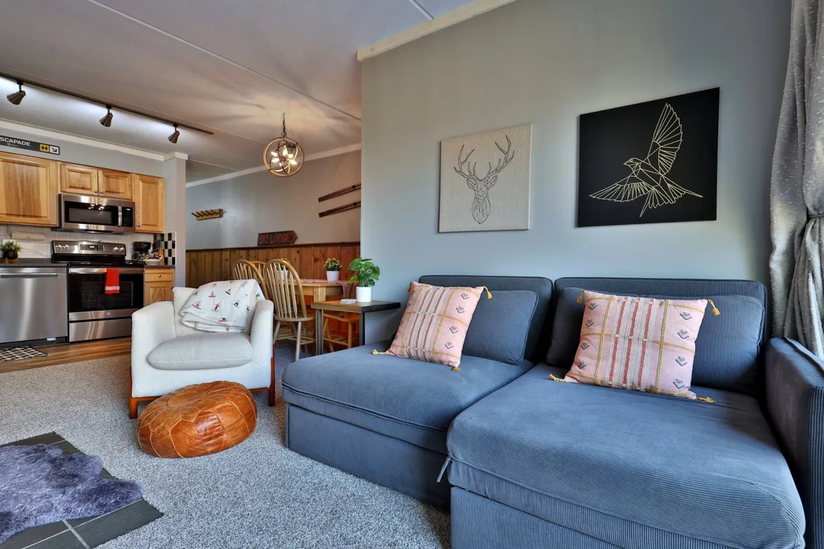 A view of the dining area and part of the living space, with a wooden dining table and chairs set beside a cozy sofa adorned with patterned cushions. Artistic wall decor adds a sense of style and warmth.