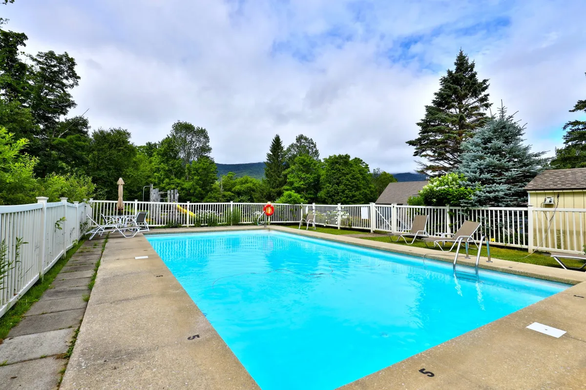 This image captures a sparkling outdoor swimming pool surrounded by lush greenery and comfortable poolside lounge chairs. The inviting water and tranquil setting evoke a sense of leisure and relaxation. The scene is bathed in natural light, highlighting the refreshing atmosphere and ample space for both swimming and sunbathing.