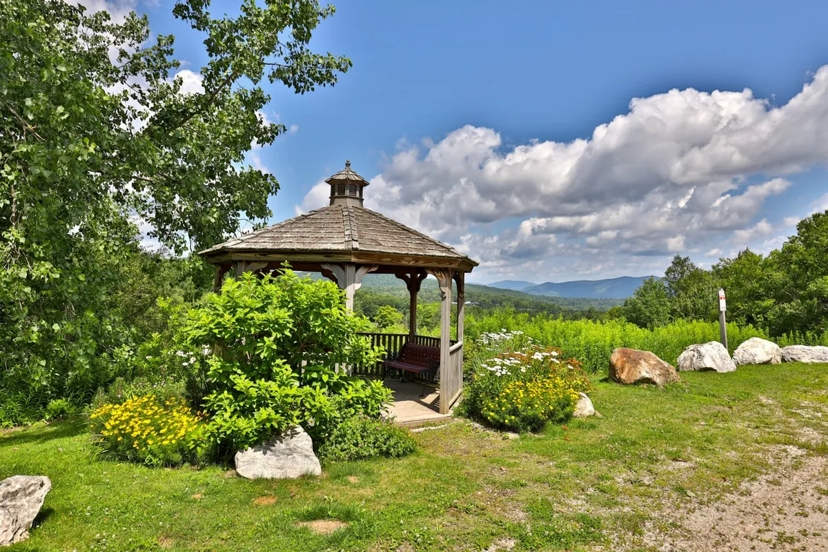 A peaceful garden scene featuring a charming gazebo, surrounded by blooming wildflowers and a sweeping landscape. The setting offers a tranquil spot to unwind and soak in the beauty of Killington.