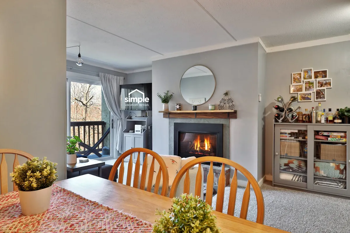 The image showcases a warm and inviting interior with a cozy fireplace as the centerpiece, a dining table perfect for shared meals, and a comfortable seating area bathed in soft light. The mirror reflects natural light, enhancing the sense of space, and the overall ambiance encourages relaxation and togetherness.