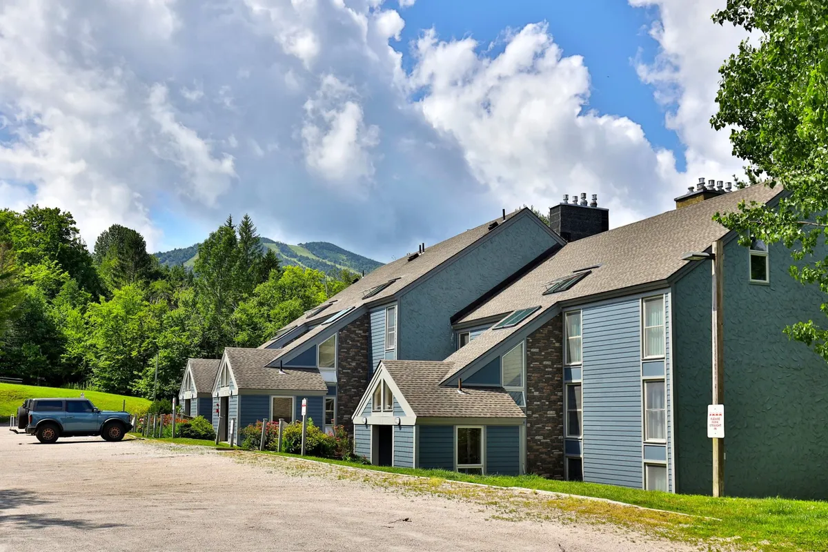 This image captures the exterior of multi-story buildings nestled against a dramatic mountain backdrop, surrounded by lush greenery. The vibrant natural setting and architectural style reflect the area's active lifestyle and scenic appeal.